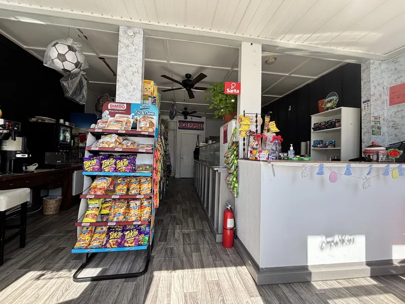 Inside Grocery La Bendición: a snack rack of Bimbo bread and Takis, the front counter, a Sarita ice cream sign and a Ricas Pupusas sign over the kitchen.